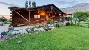 Eine Holzblockhütte mit Veranda, umgeben von einem gepflegten Garten und einem Bergpanorama.