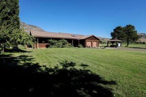 A rustic cabin with a large open porch, a covered outdoor seating area, and a well-maintained lawn.