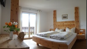 A bedroom with a wooden bed, a wooden nightstand, a bedside table with a vase of flowers, and a sliding glass door to the balcony. - Agriturismo Gfaderhof Ferienwohnungen (Bressanone)