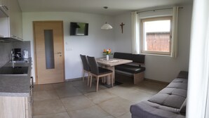 A compact kitchen with a built-in stove, a coffee maker, and a sink. There is a dining area with a table, chairs, and a bench. A TV is mounted on the wall, and a cross is visible. - Agriturismo Gfaderhof Ferienwohnungen (Bressanone)