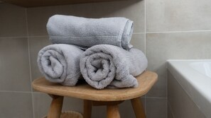 Una pila de toallas grises sobre un taburete de madera en un baño con paredes de azulejos.