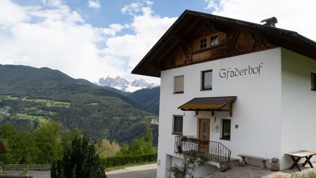 A white building with a wooden roof and balcony, labeled "Gfaderhof," set against a mountainous backdrop. - Agriturismo Gfaderhof Ferienwohnungen (Bressanone)