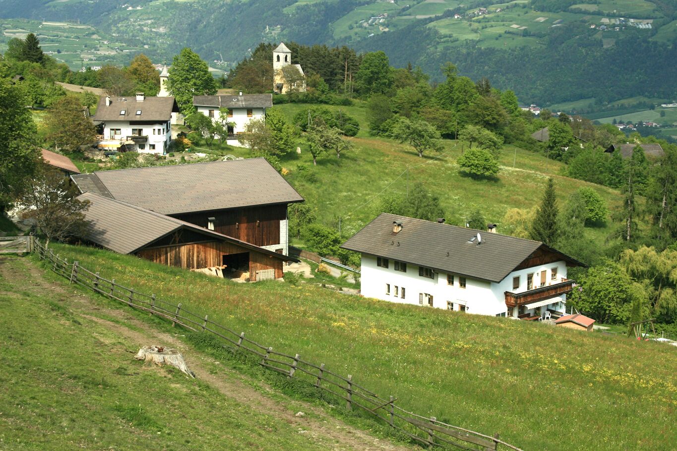 Une maison de campagne dotée d’un toit en pente, entourée d’une végétation luxuriante et située dans un paysage vallonné.