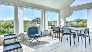 Tilava huone, jossa on suuret ikkunat, ruokapöytä ja modernit tuolit.
