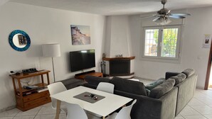 A living room with a TV, sofa, dining table, and chairs.