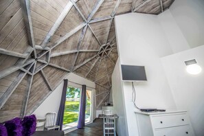 A room with a sloped ceiling, a flat-screen TV mounted on the wall, a desk with a chair, and a window with a view of greenery outside. - STUDIO 02 - Lake Sumner (Clermont)