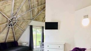 Ein Schlafzimmer mit schrägverdeckter Decke, einem Bett, einer Kommode und einem an der Wand befestigten Fernseher.