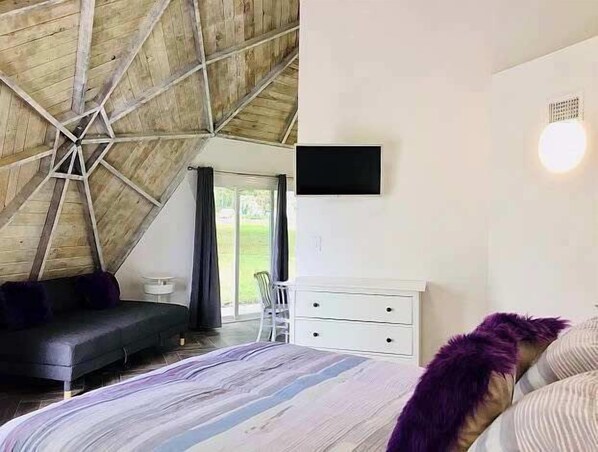 A bedroom with a sloped ceiling, a bed, a dresser, and a television mounted on the wall. - STUDIO 02 - Lake Sumner (Clermont)