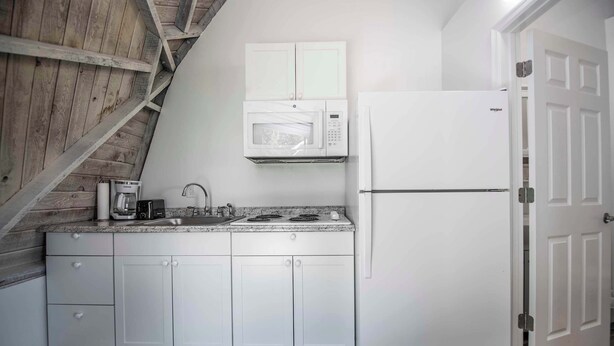 A kitchen with white cabinets, a microwave, a stove, and a refrigerator. - STUDIO 02 - Lake Sumner (Clermont)