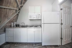 A kitchen with white cabinets, a microwave, a stove, and a refrigerator. - STUDIO 02 - Lake Sumner (Clermont)