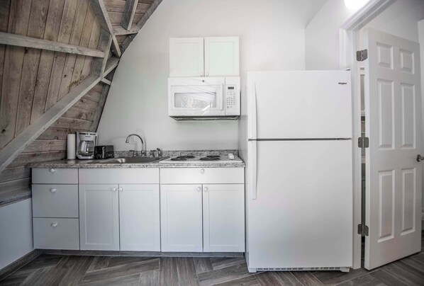 A kitchen with white cabinets, a microwave, a stove, and a refrigerator. - STUDIO 02 - Lake Sumner (Clermont)