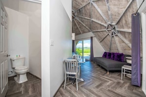 A room with a wooden ceiling, a toilet, a dining area with chairs, a sofa, and a view of the outdoors. - STUDIO 02 - Lake Sumner (Clermont)