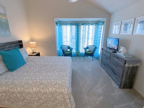 A bedroom with a bed, a dresser, a TV, and a small table with chairs.