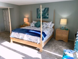 Et soveværelse med himmelseng, et natbord med lampe, en kommode og et billed på væggen.
