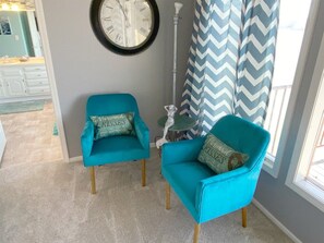 A room with two teal armchairs, a round wall clock, a small table, and a chevron-patterned curtain.