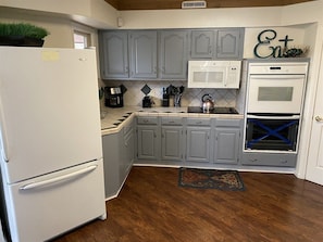 A kitchen with grey cabinets, a white refrigerator, a microwave, and an oven.