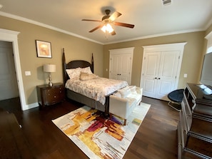 A bedroom with a bed, nightstands, a dresser, a ceiling fan, and a large window.