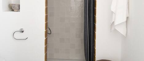 Ducha con pared de azulejos, un taburete de madera y un perchero.