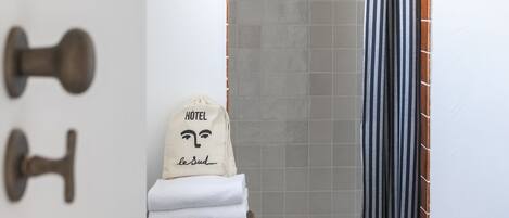 Un baño con ducha, un perchero con toalla y un taburete de madera.