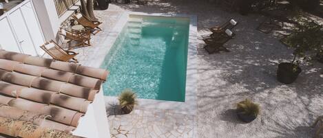A rectangular swimming pool with clear water, surrounded by a tiled deck and outdoor furniture.