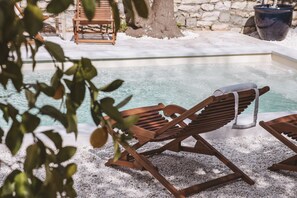 A wooden lounge chair by a pool with a stone wall and a tree in the background. - Hôtel le Sud (Antibes)