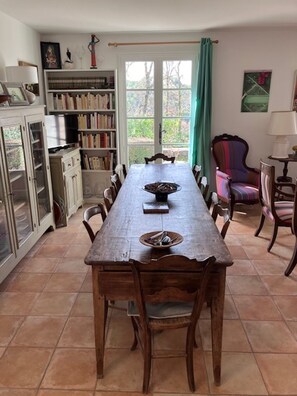 A dining area with a long wooden table, chairs, and a bookshelf.