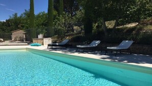 A swimming pool with clear water, surrounded by lounge chairs and a stone wall. -  Air Conditioning House with character located  in Luberon (Ménerbes)