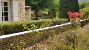 A stone building with a tiled roof, surrounded by lush greenery and a well-maintained hedge. -  Air Conditioning House with character located  in Luberon (Ménerbes)