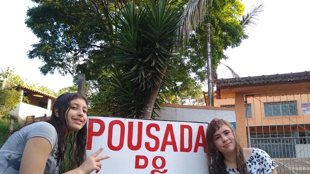 Two people standing in front of a sign that reads "POUSADA DO JOÃO". - Pousada do joao (Juiz de Fora)