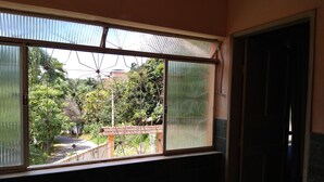 A room with a large window overlooking a garden area with a pathway and a small structure. - Pousada do joao (Juiz de Fora)