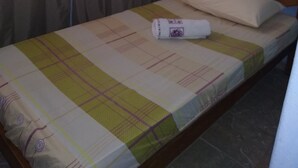 A single bed with a patterned bedspread, a rolled-up towel, and a wooden headboard in a room with a window and curtains. - Pousada do joao (Juiz de Fora)