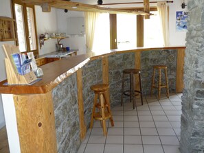 Enjoy cooking and dining in this kitchen with a wooden bar counter and stools, a stone wall, and a window with curtains.