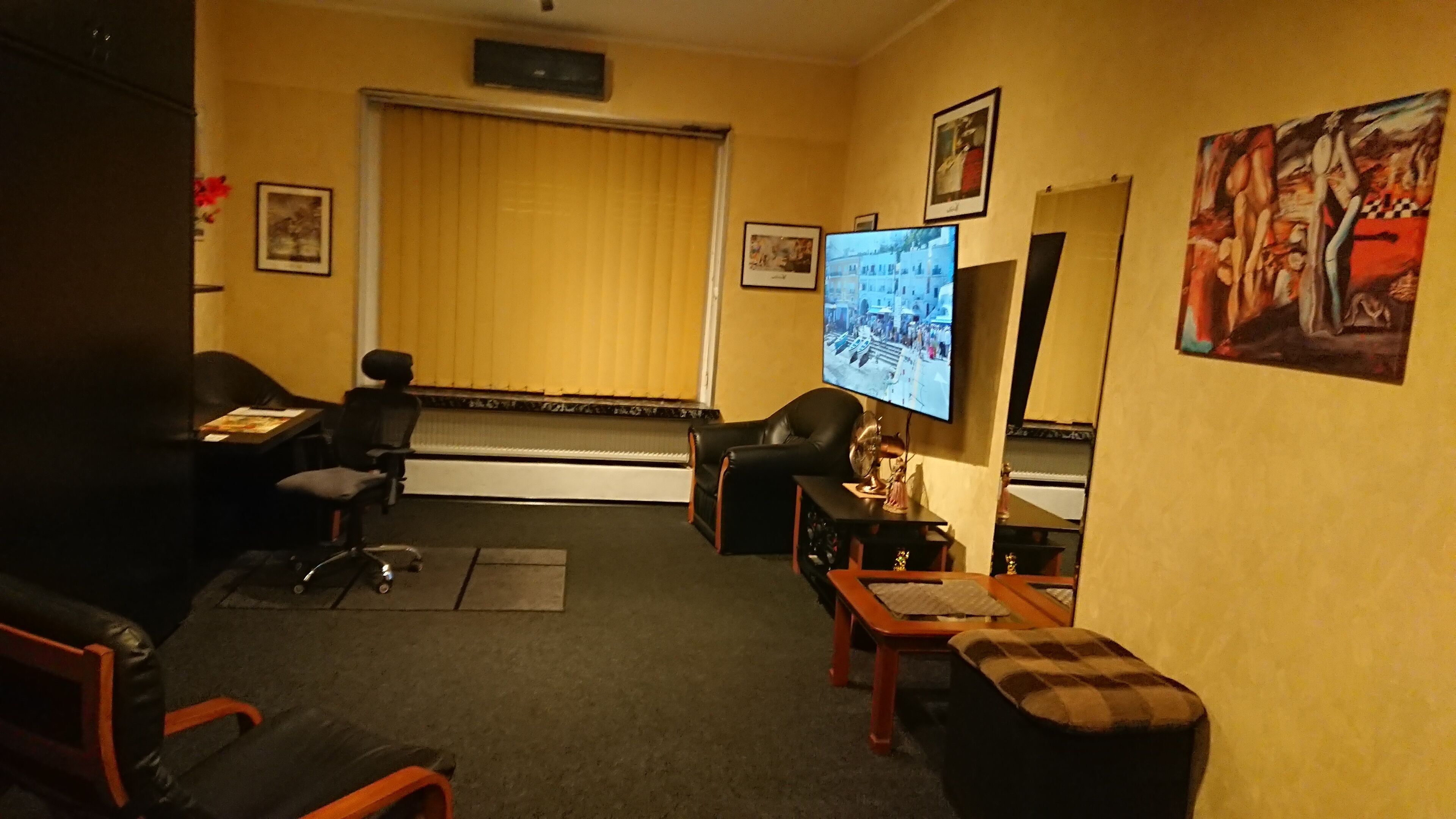 Une chambre d’hôtel équipée d’un grand téléviseur à écran plat, d’un canapé, d’un fauteuil, d’une petite table et d’une fenêtre avec des stores.