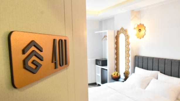 A hotel room with a bed, a wardrobe, a mirror, and a wall-mounted sign with a logo. - Avcilar Garden Hotel (Istanbul)