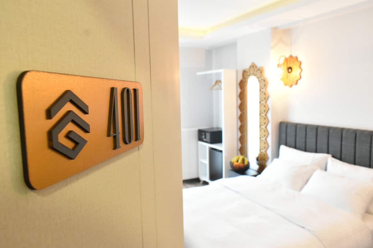 A hotel room with a bed, a wardrobe, a mirror, and a wall-mounted sign with a logo.