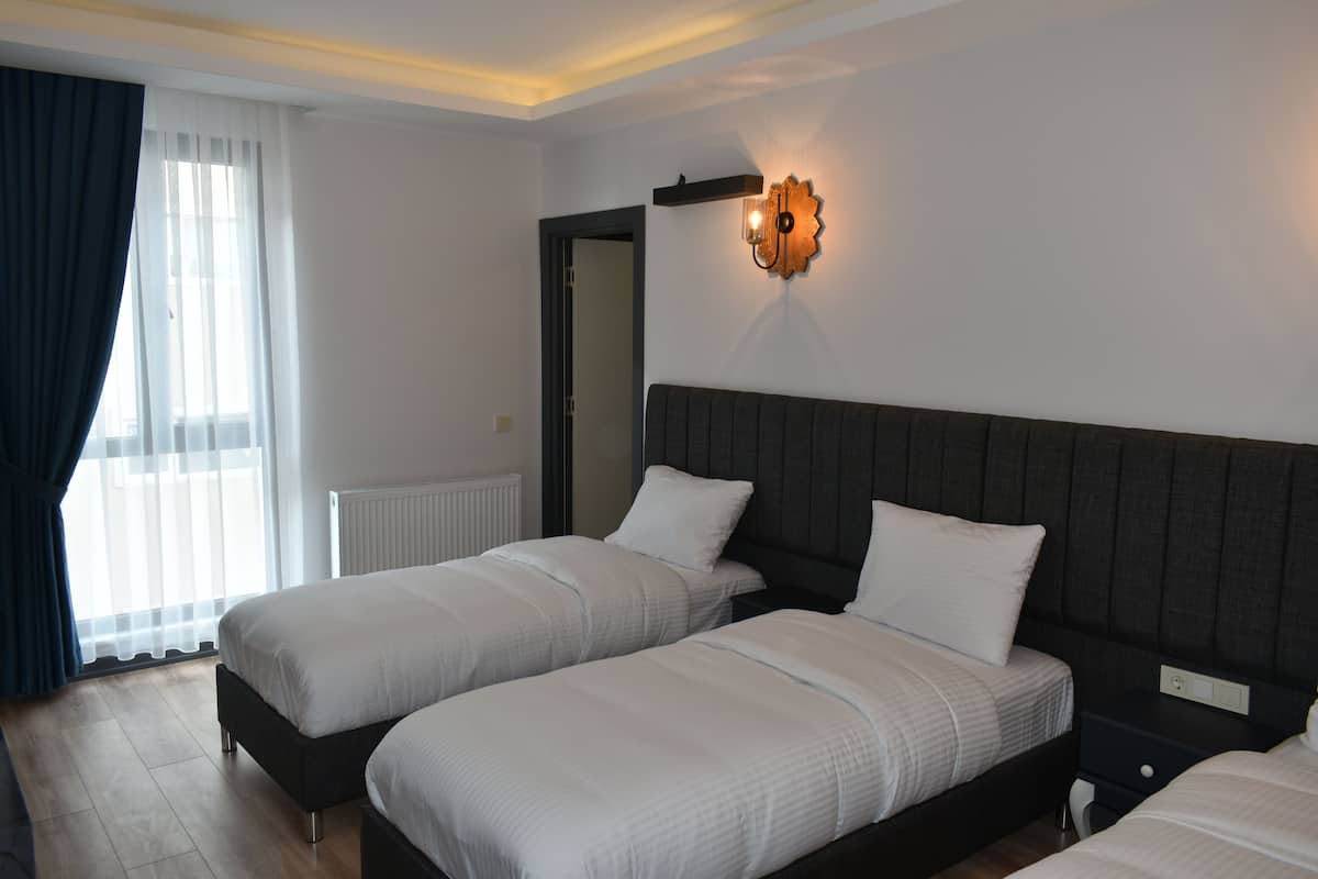 A hotel room with two beds, a nightstand, a wall-mounted light fixture, and a window with curtains.