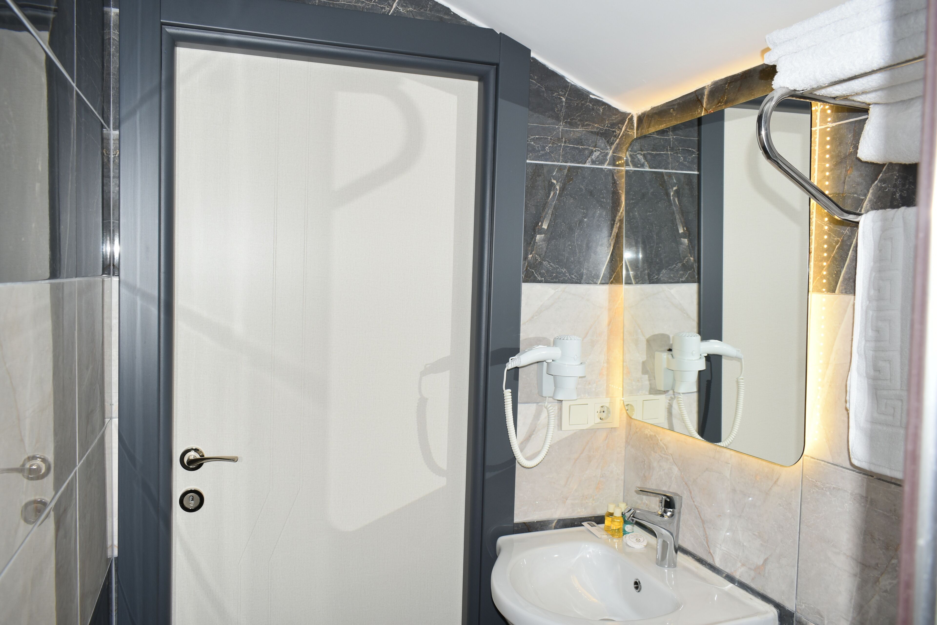 A bathroom with a glass shower enclosure, a white sink with a mirror above it, and a towel rack with a towel.