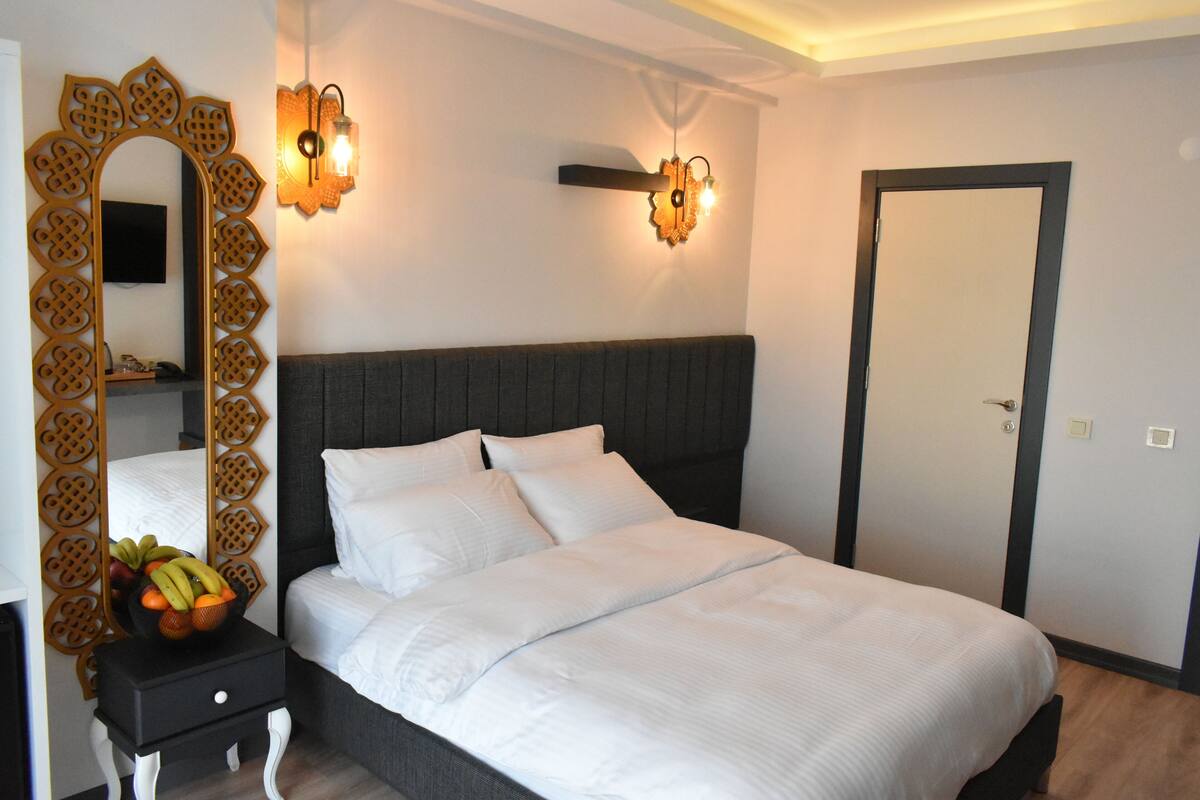 A neatly made bed with white linens, a decorative mirror, and a fruit bowl on a bedside table.