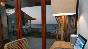 Un ordinateur portable est posé sur une table en bois, et une porte vitrée offre une vue sur l’océan.