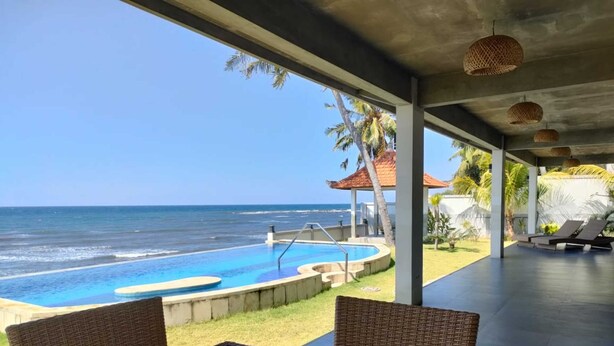 Un espace piscine avec vue sur l’océan, des meubles en osier et un patio couvert.