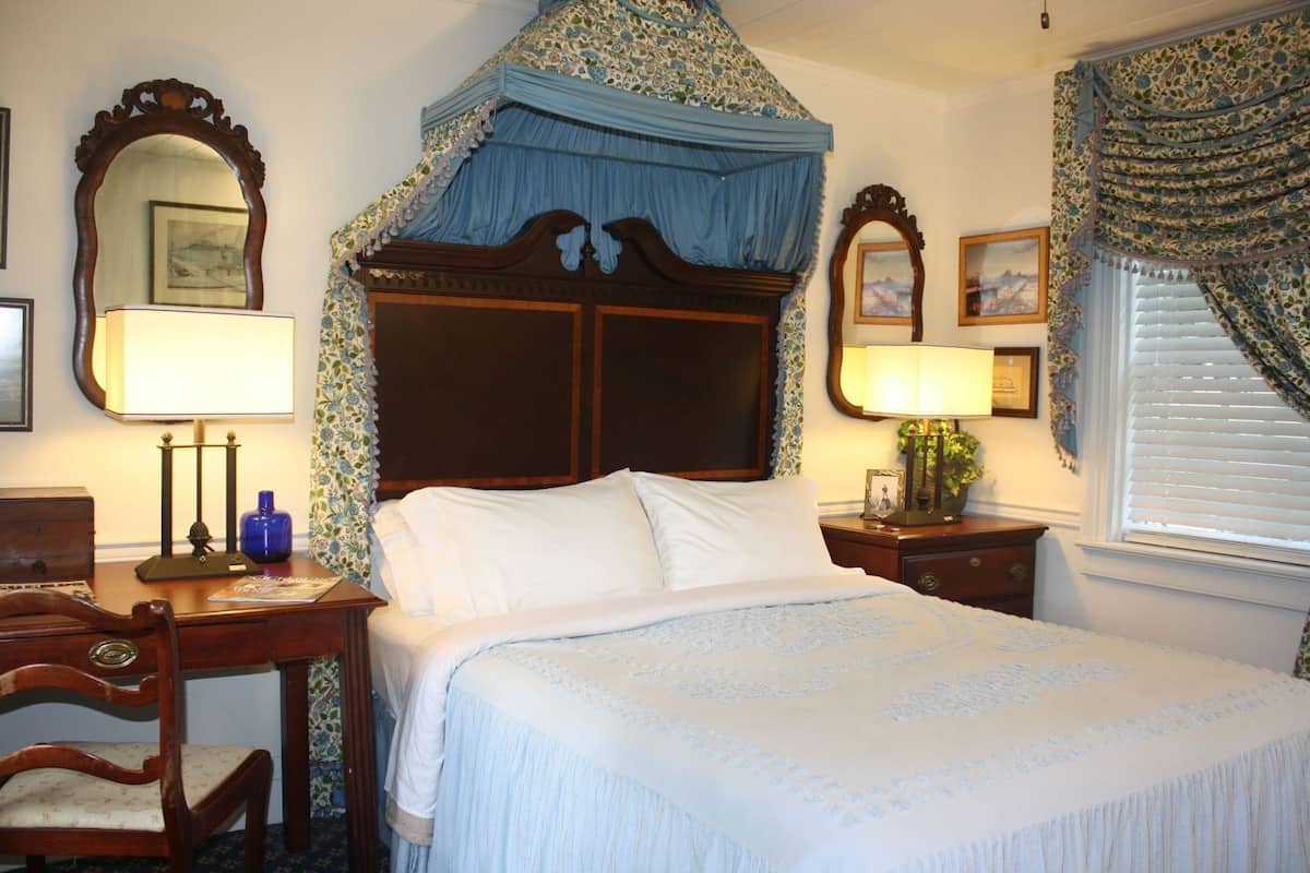 A bedroom with a four-poster bed, two bedside tables with lamps, a wooden desk, and a chair.