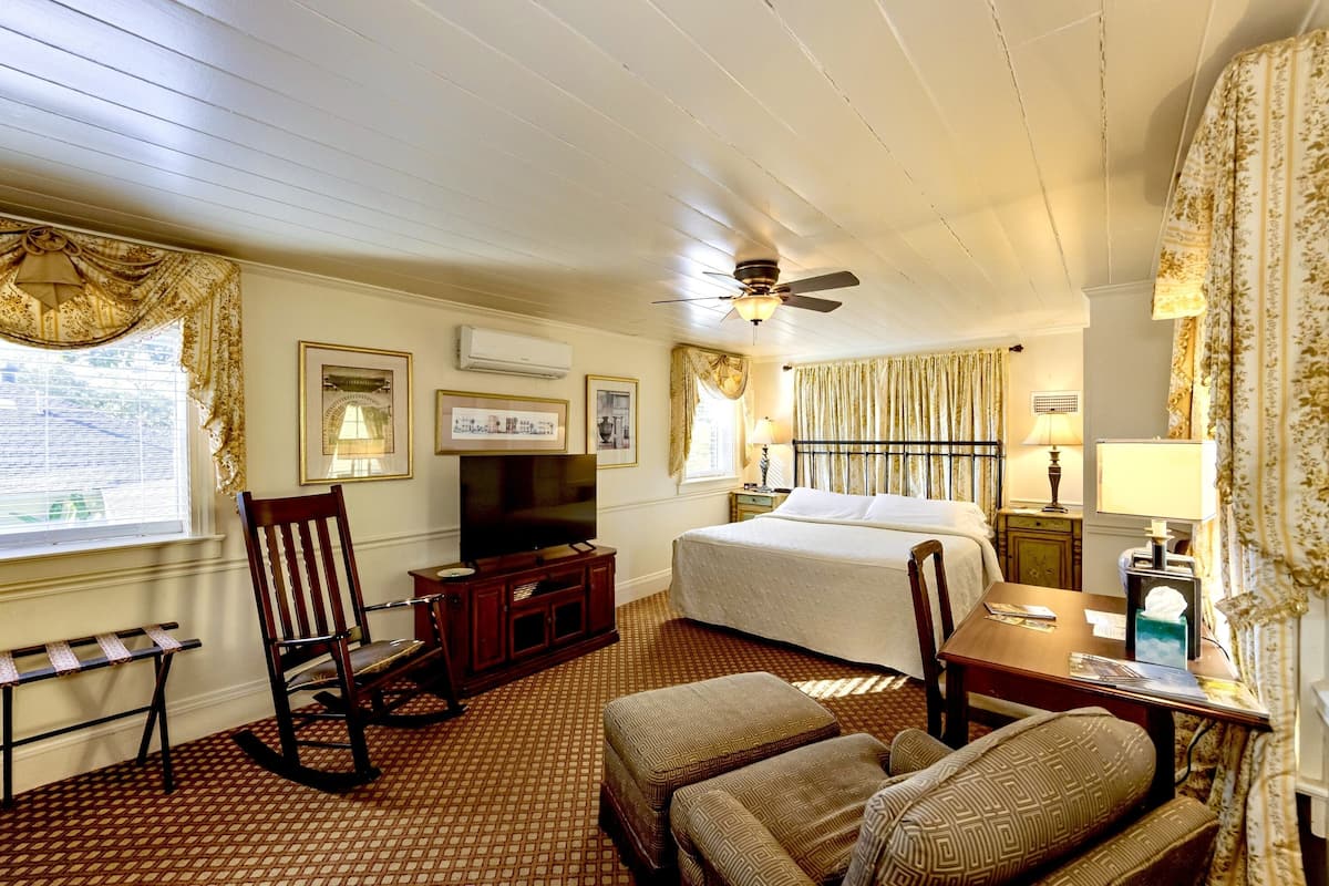 A hotel room with a bed, a television, a desk, a chair, and a window with curtains.