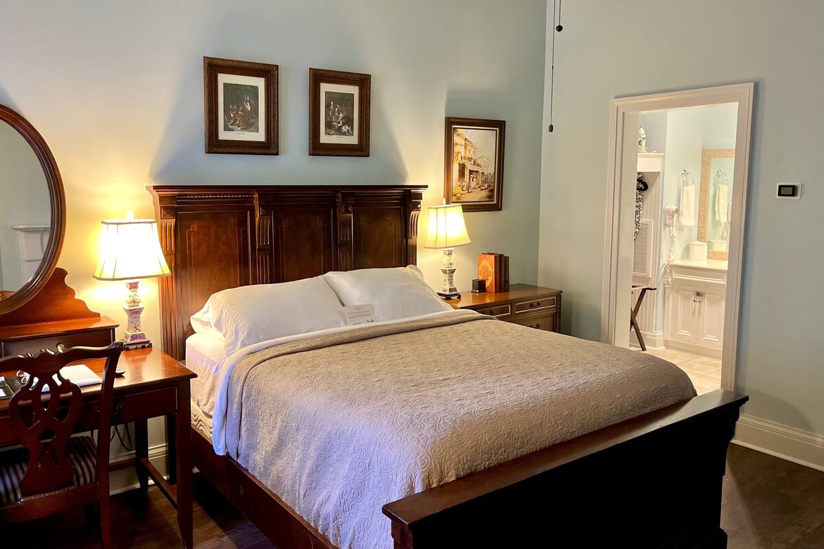 A bedroom with a large bed, a wooden nightstand with a lamp, a dresser, and a mirror. There are two framed pictures on the wall above the bed.