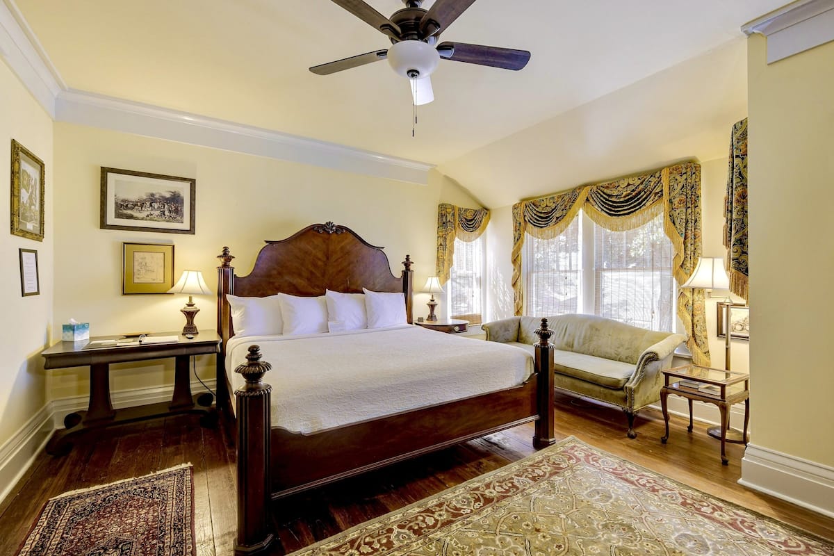 A spacious bedroom with a large bed, a wooden headboard, a ceiling fan, and a classic design.