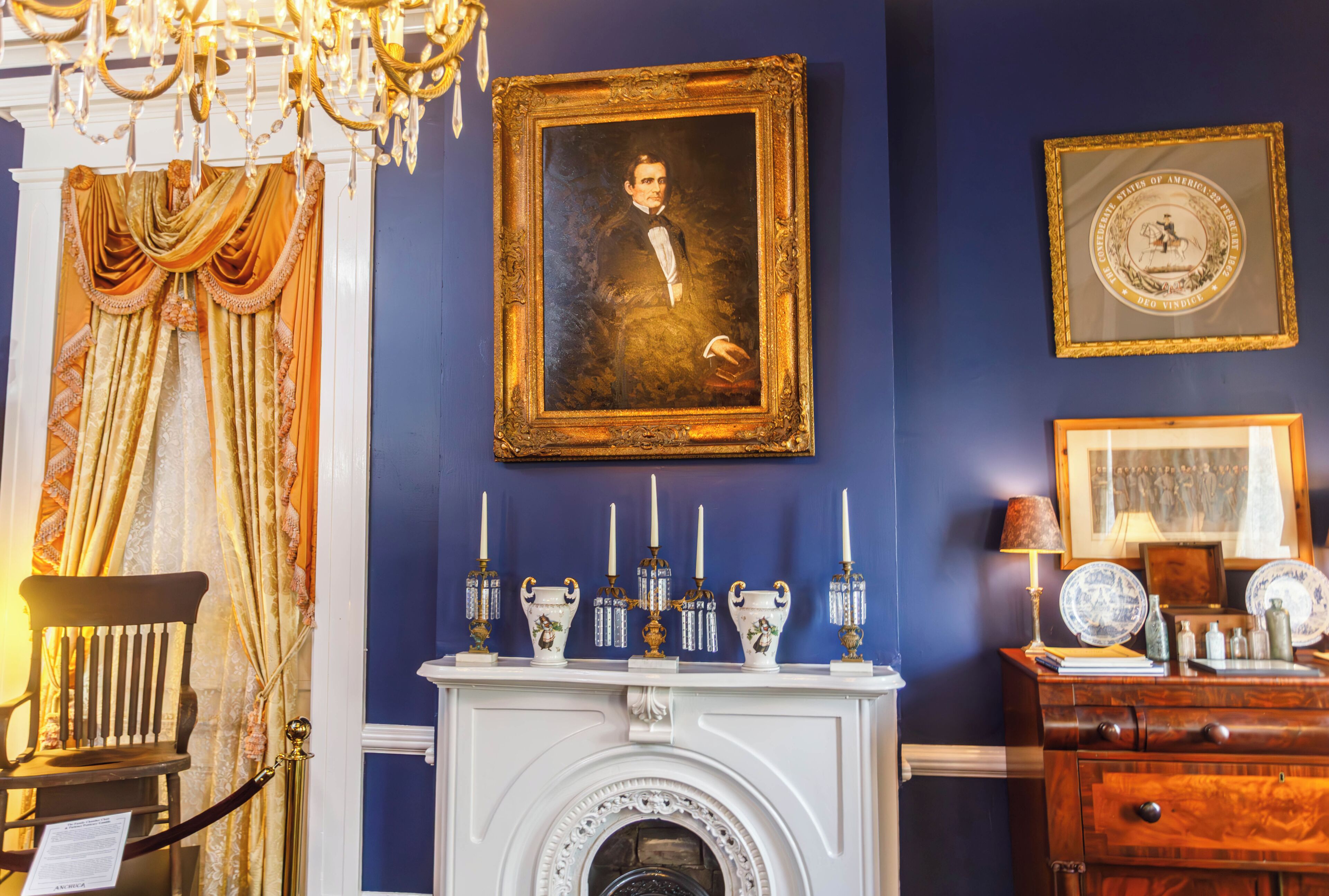 A room with a fireplace, a framed portrait, and a chandelier.