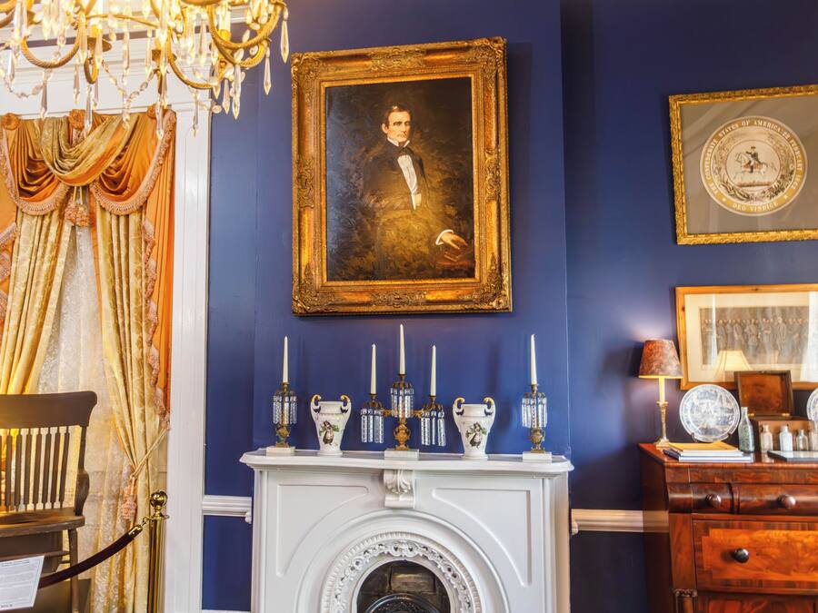 A room with a fireplace, a framed portrait, and a chandelier.
