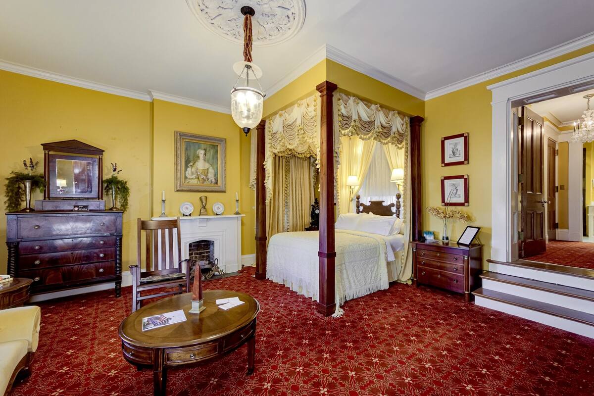 A traditional bedroom with a four-poster bed, a wooden dresser, a round table, and a mirror.