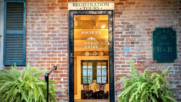 A brick building with a registration and tours sign, a guest entry door, and a plaque indicating the building's history. - Anchuca Historic Mansion & Inn (Vicksburg)