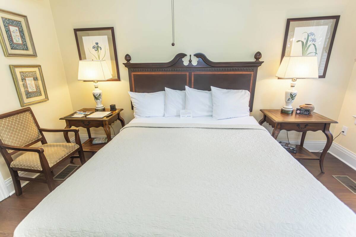 A hotel room with a large bed, two bedside tables with lamps, a chair, and framed pictures on the walls.