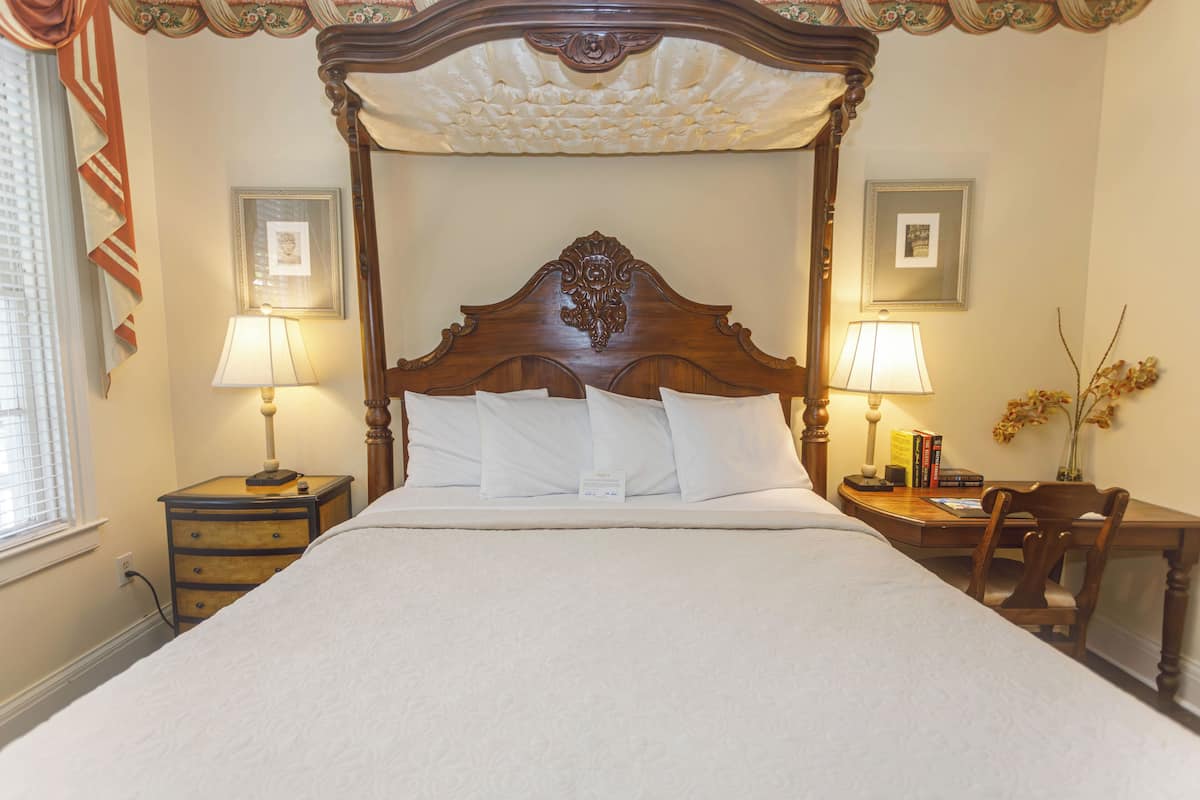 A four-poster bed with a wooden headboard, two bedside tables with lamps, and a chair at the foot of the bed.